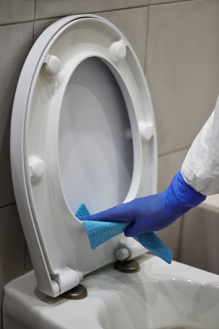 Close-up of a hand in gloves disinfecting a toilet with a blue cloth.