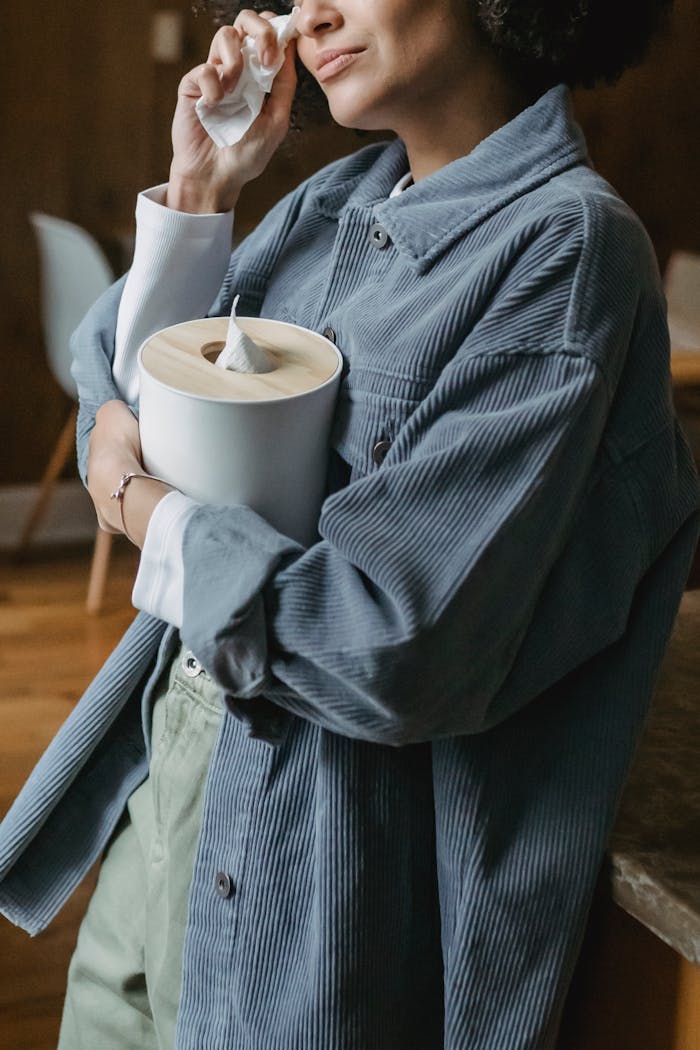 Crop disappointed African American female wiping tears with tissue while standing near table and crying